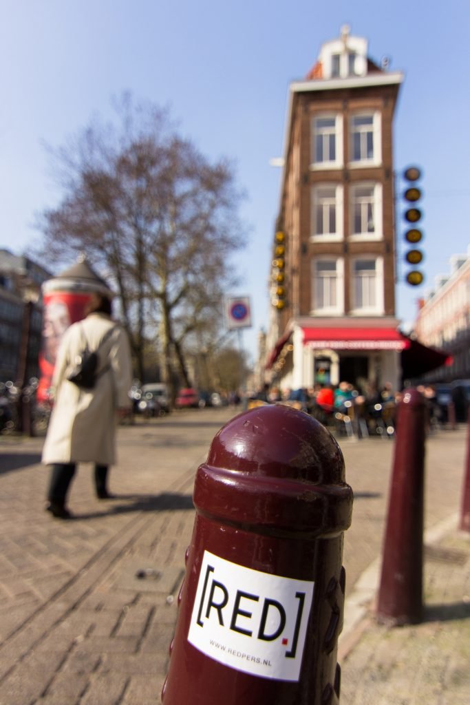 In een Amsterdamse fotoreportage kan het Amsterdammertje natuurlijk niet ontbreken. Overal door de stad staan deze paaltjes om auto’s van de stoep of, zoals hier, van het terras te weren.